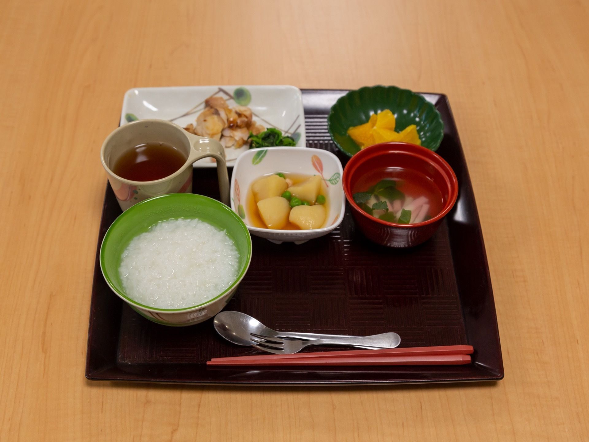 おかゆを主食とした食事である。主菜のほか、小鉢が２つとお吸い物とお茶、箸とスプーンとフォークがお盆にのっている。