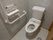 Ｌ字型の手すりが備えられたトイレである。トイレットペーパーホルダーの上にリモコンがあり、壁の低い場所に緊急時呼出しボタンが設置されている。