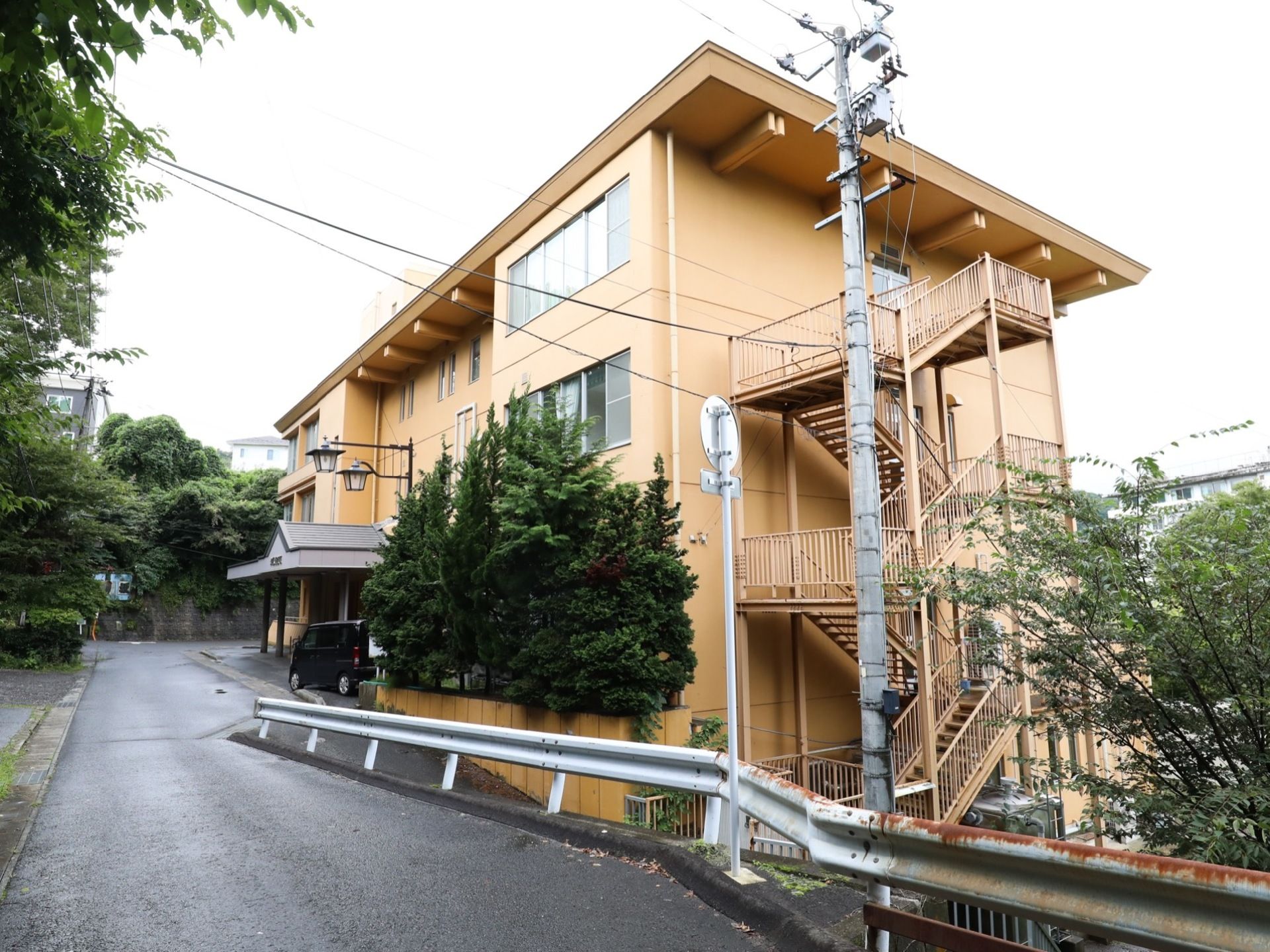 施設の外壁はベージュ色で、４階建ての建物となっている。右側には、施設と同じ色の屋外階段が設置されている。