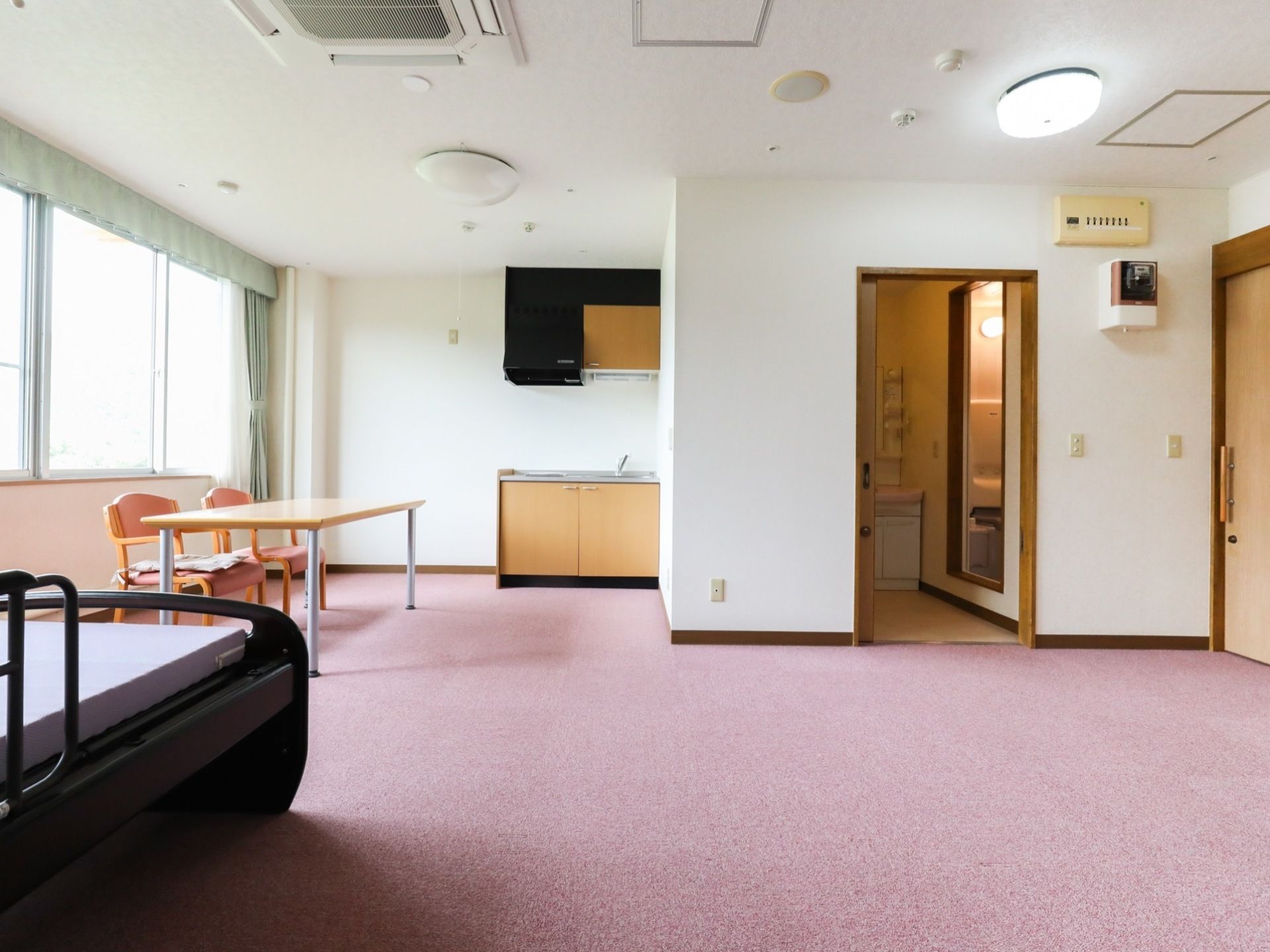 入居者様用の居室は広く、キッチンや浴室、脱衣所など生活に必要な設備が整っている。窓際には、テーブルやベッドなどの家具も置かれている。