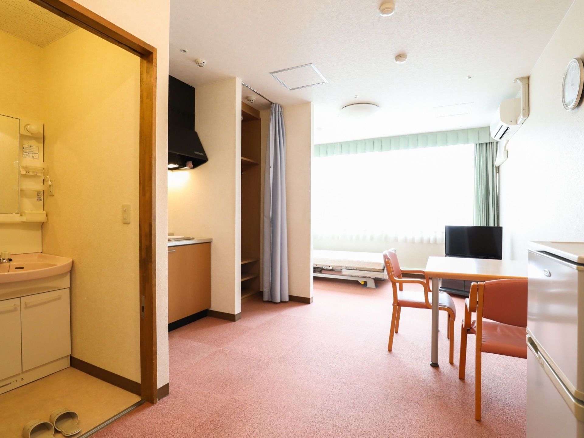 居室はゆったりとした広さがあり、左側に浴室や洗面所、キッチンなどの設備が並んでいる。右側には、テーブルや冷蔵庫が置かれている。
