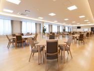 広々とした窓が複数設置された食堂である。円型と正方形のテーブル、背もたれ椅子がバランスよく配置されている。