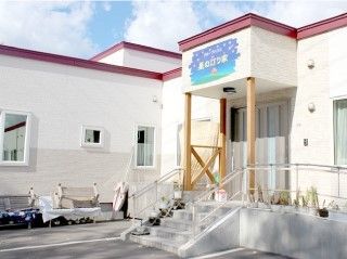 ホームの外観。平屋建ての建物は白く、エンジ色の屋根。玄関前にはスロープも設置されている。