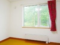 シンプルな居室は白い壁にフローリングを使用。大きな窓には赤いカーテンが付けられている。