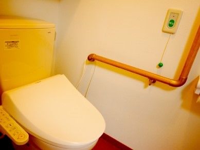 呼び出しボタンやエル字型の手すりが設置されたシンプルなトイレ。
