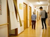 廊下を歩く女性入居者と男性スタッフ。二人が並んで話をしながら歩いている様子。