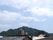 青い空の下、高層マンションや民家がある住宅地があり、その向こう側に山が見えている。