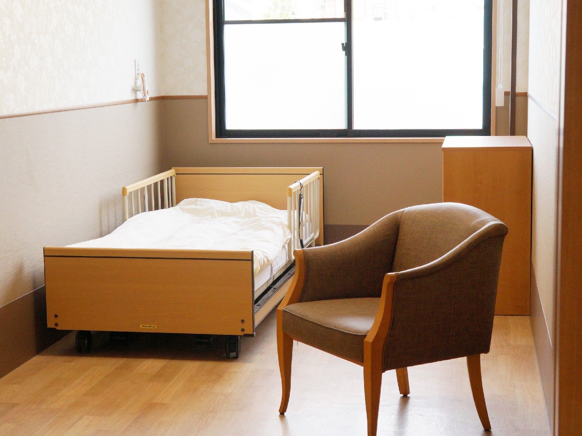 大きな窓がある明るい居室にはベッドやいす、収納家具などが置かれている。
