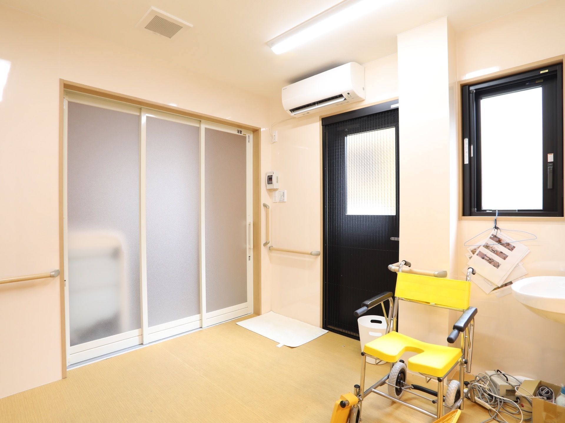 エアコンが付いた小部屋があり、曇りガラスの引き戸がある。木目調のビニール床に、黄色い車椅子がある。
