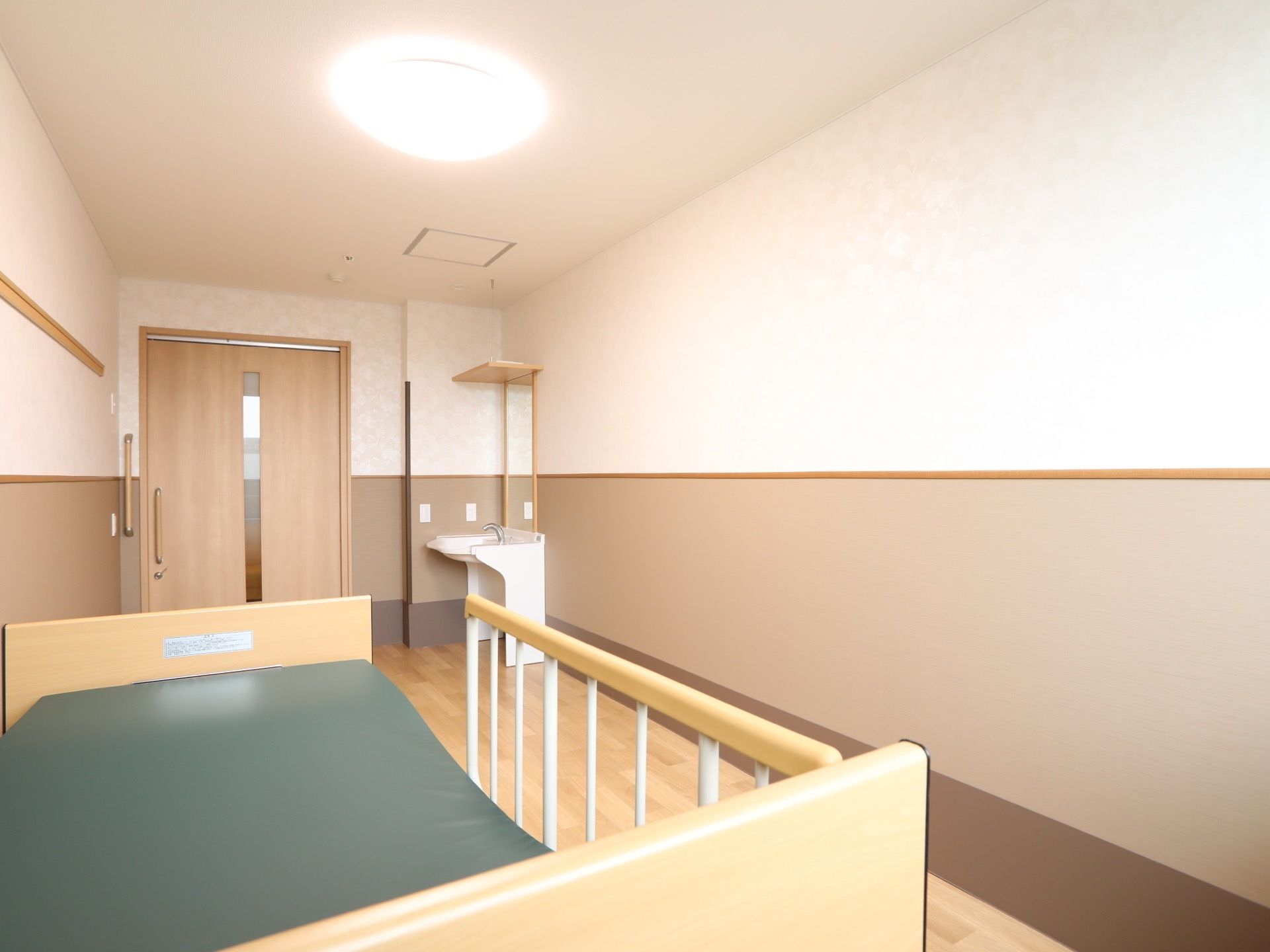 居室を入るとすぐに洗面台がある。部屋は奥行きがあり、ベッドの他に収納家具などが置けるスペースがある。