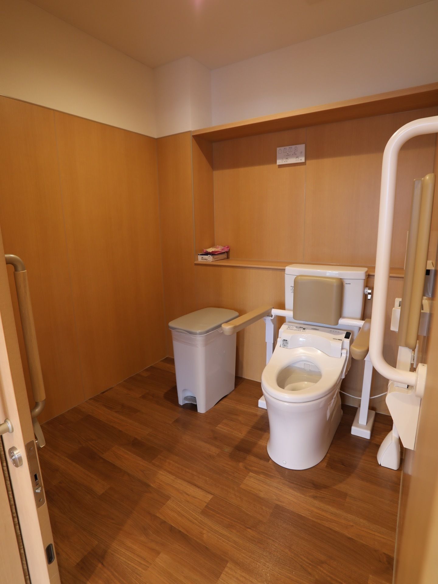 フローリングと木目調の壁が使われていて、温かな印象のトイレがある。便座の両脇や壁には手すりがある。