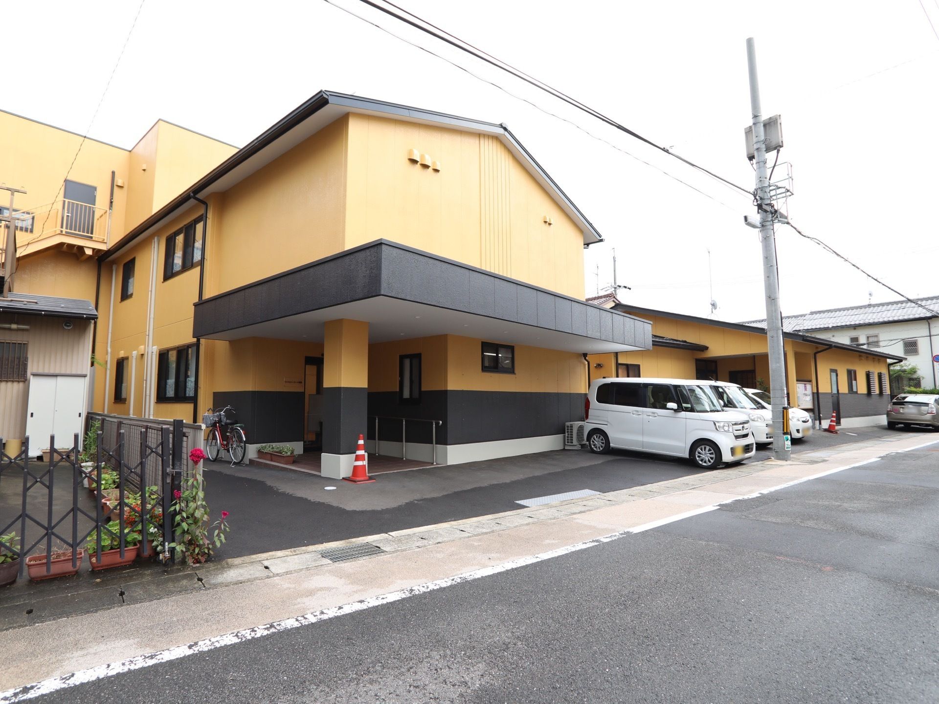 黒とクリーム色の2色の外壁が印象的な建物がある。建物の前は駐車スペースになっていて、道路は道幅が広くなっている。