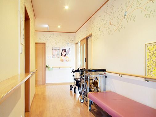 手すり付きの廊下に椅子と車いす、歩行補助器具が置いてある。介護仕様の施設内