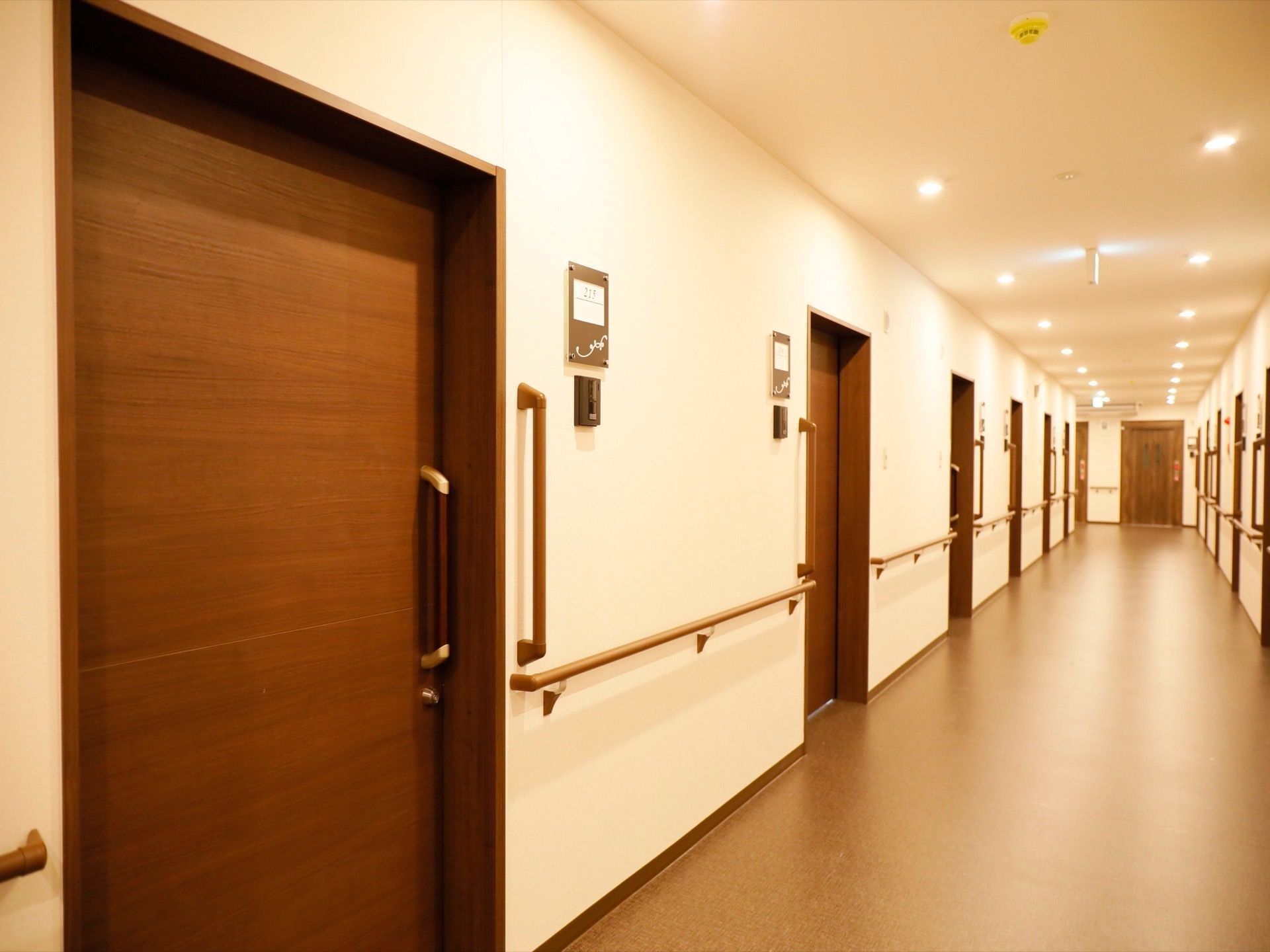引き戸が並んだ通路は幅が広くなっている。横にも縦にも手すりが備えつけられており、居室一つ一つにインターホンや表札がついている。