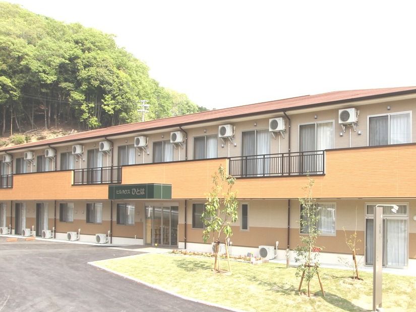 2階建ての建物は横に長く、中央に玄関が見える。建物周辺には木が植えられている。