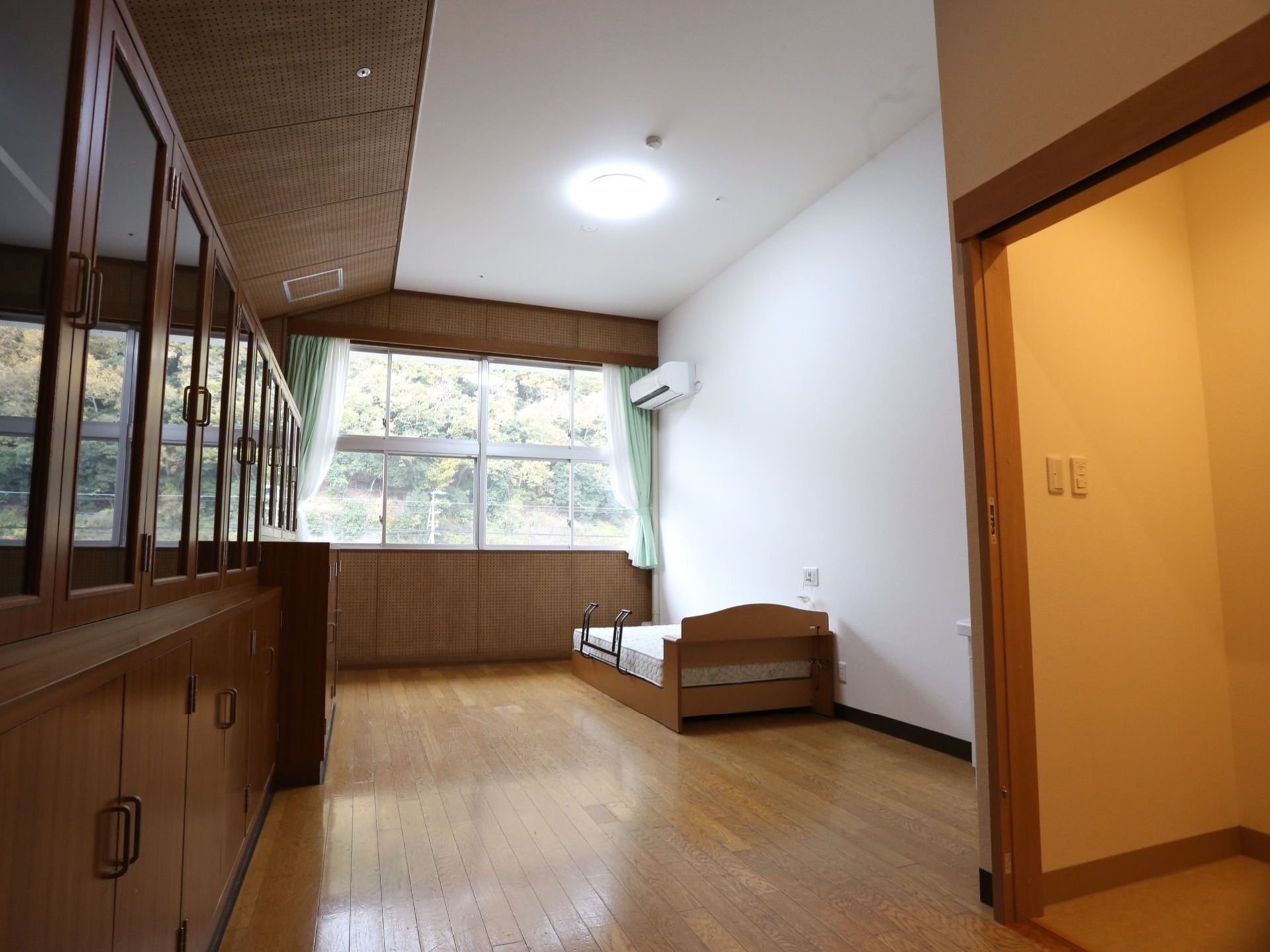 右手にトイレへの入口があり、奥の居住スペースにベッドが置かれている。窓からは近隣の自然が眺められる。