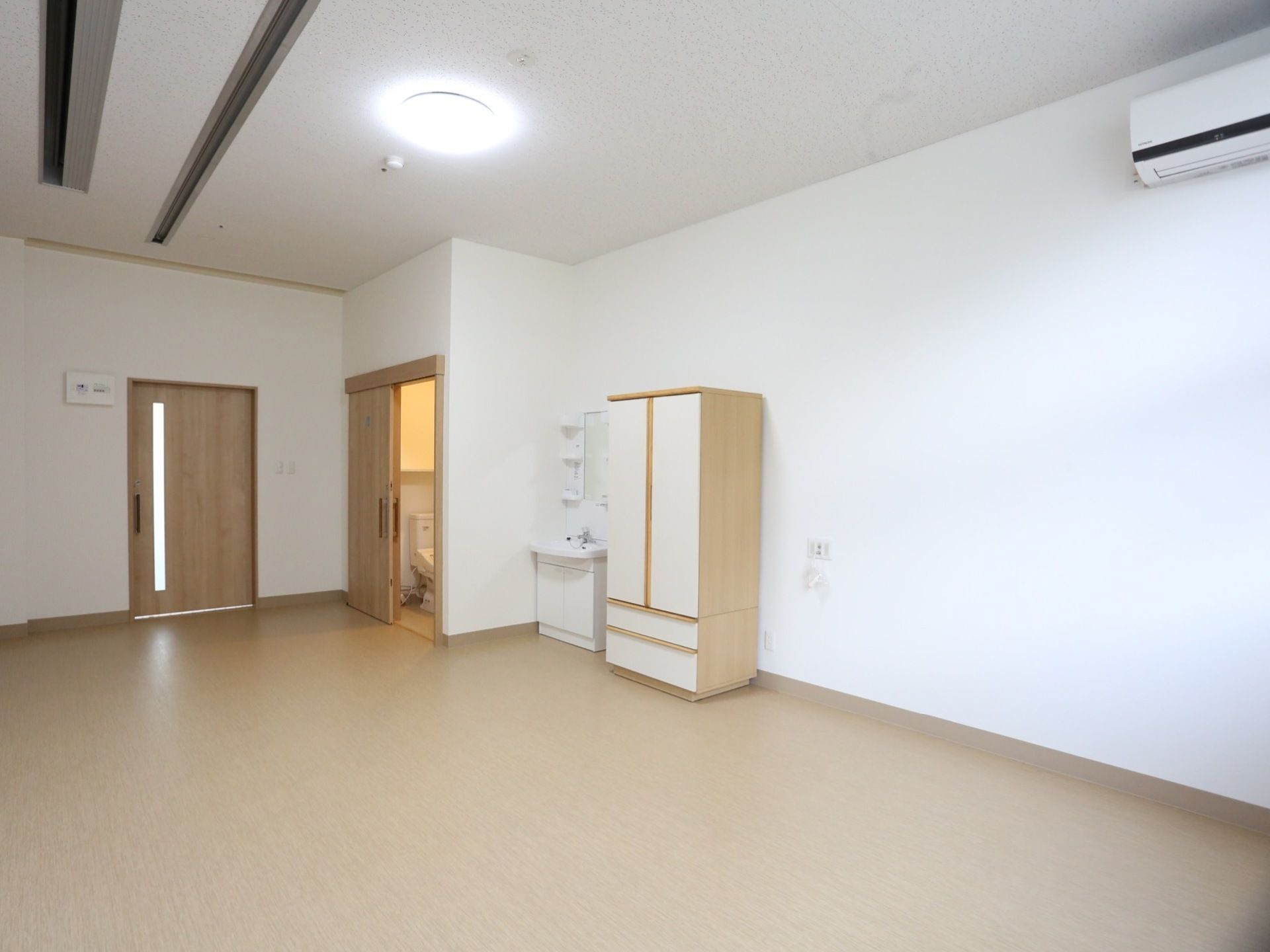 フローリングの床に白い壁の部屋で、入り口横にトイレがある。トイレの前には洗面台と洋タンスが置かれている。