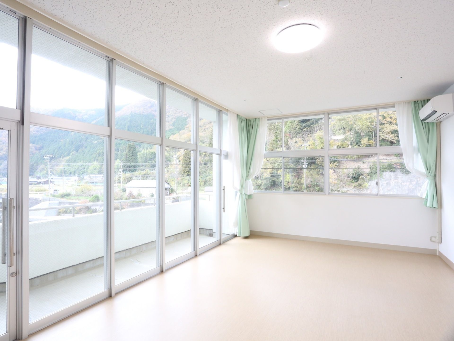 角部屋はL字型に窓があり、左手にある窓はベランダに出られる大きなサイズのものである。外は近隣の山々が見えている。