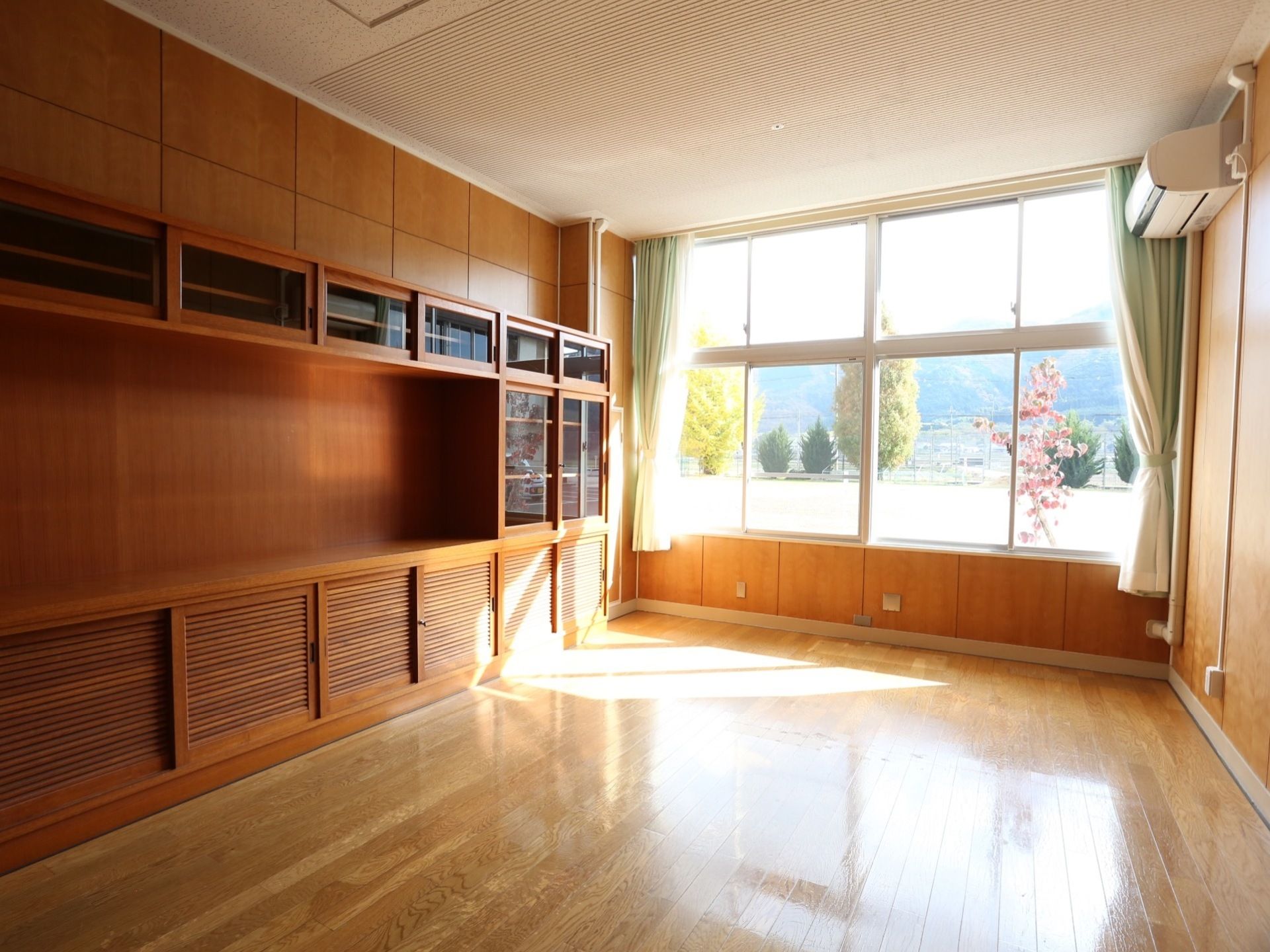 全面に木材を使用した居室で、奥側は一面が窓になっている。左の壁は作りつけの棚が並び、ガラスの引き戸が閉まっている。