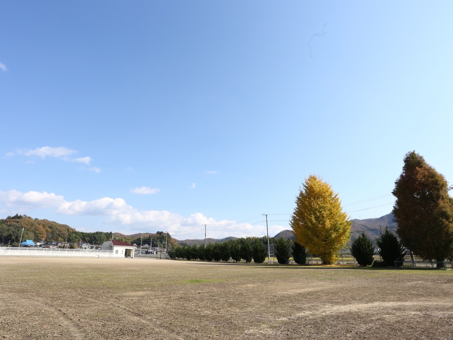 施設の前は広い空き地になっている。大きな木が２本生えており、その向こうには山並が連なっている。周囲に高い建物がない。