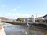 施設の前に川が流れている。川の向こうには住宅地が広がっている。左手奥には高い山が連なっているのが見える。