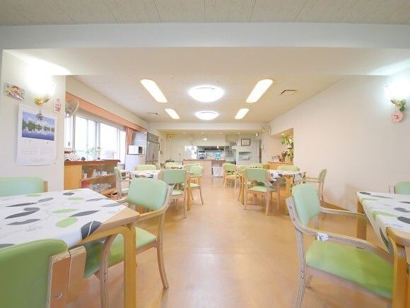 空調設備が整った開放的な食堂で、壁にはテレビや戸棚が設置されている。ダイニングテーブルや椅子が複数配置されている。
