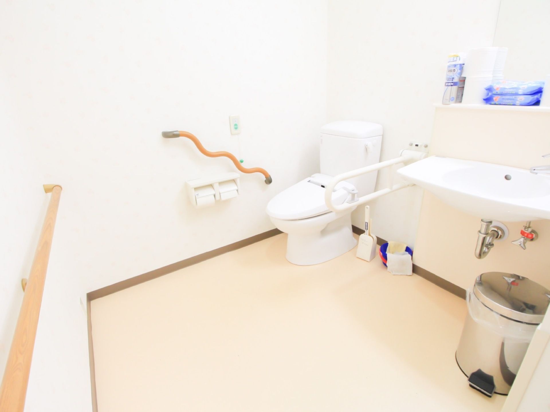 トイレは広々としており、手すりが随所に備わっている。トイレットペーパーや清掃用具が棚に置かれており、足元がスッキリしている。