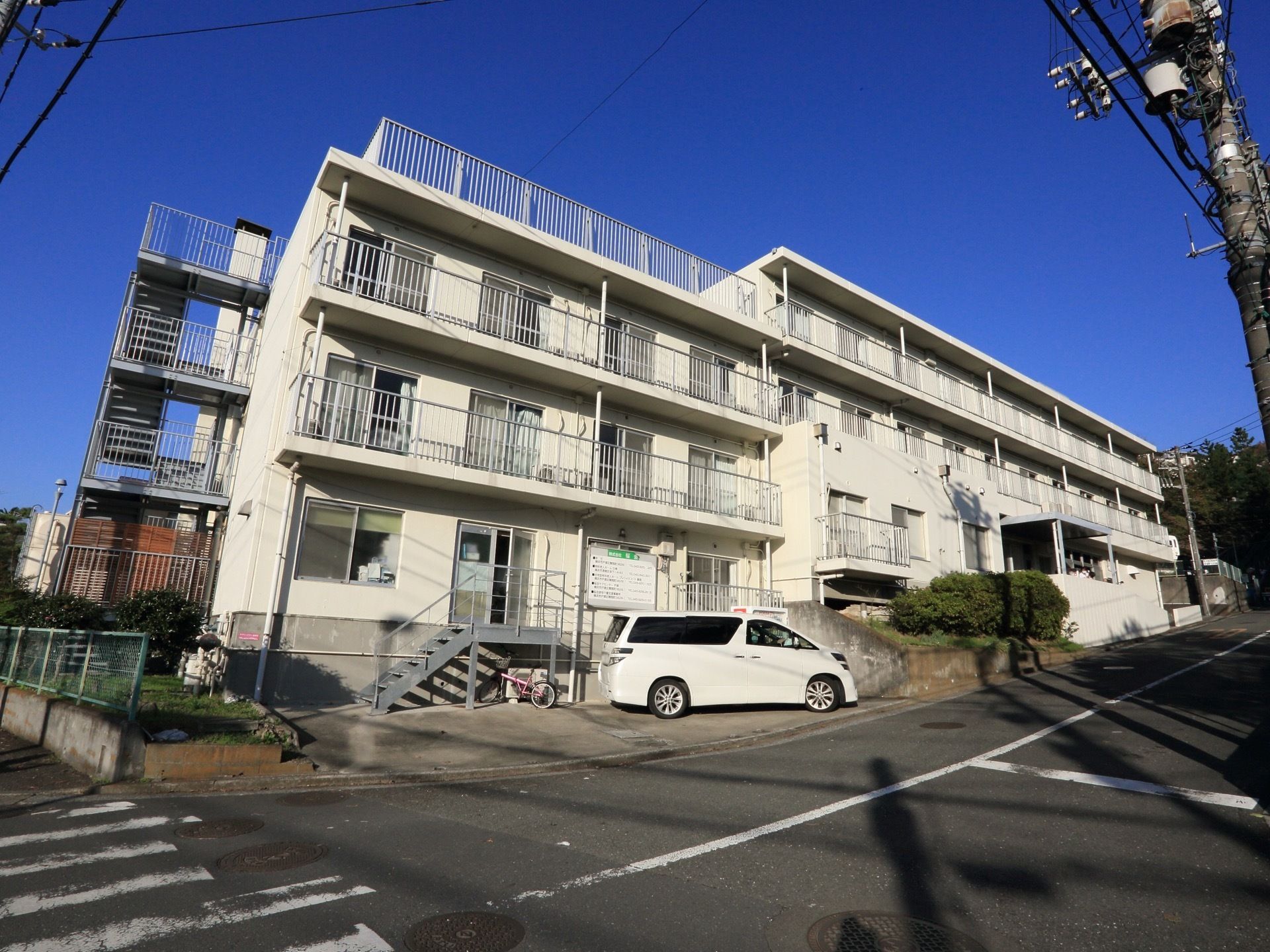 坂道の小高い位置にある、四階建ての大きな建物がある。居室のベランダがあり、建物脇には非常階段が設置されている。