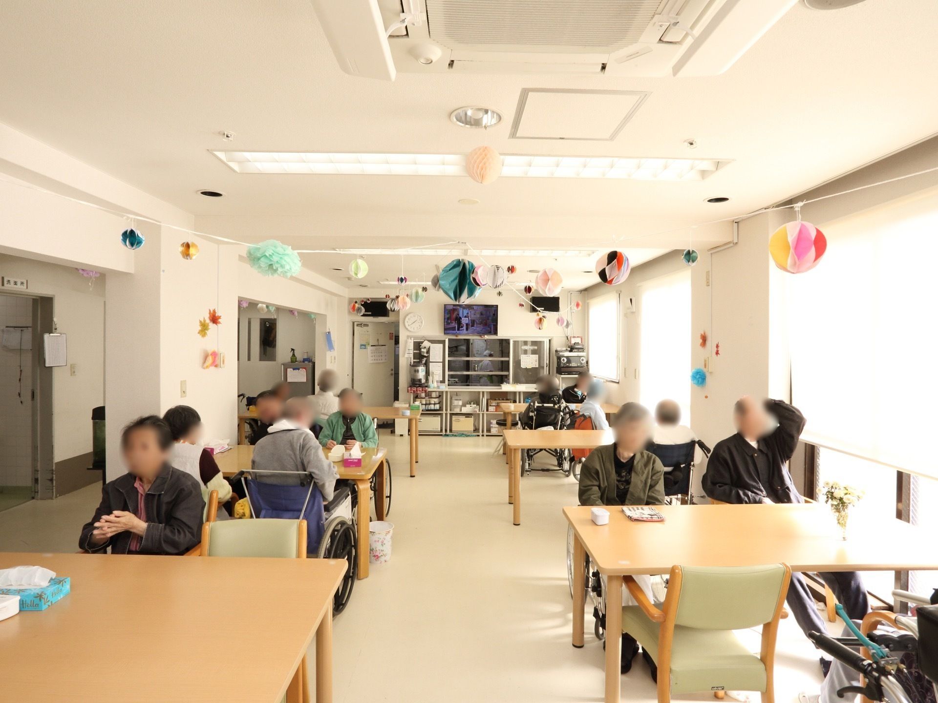 大きな窓が設置され、明るい共有スペースでくつろいでいる入居者様