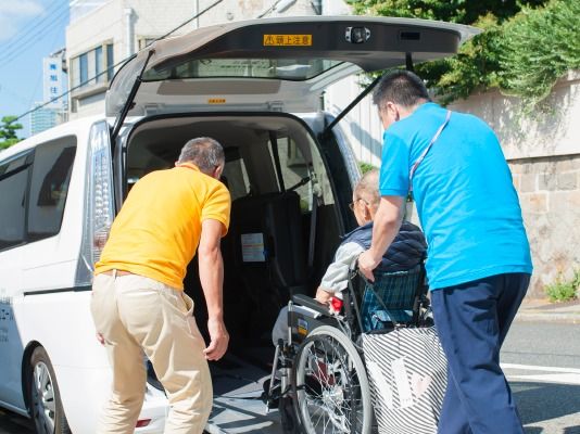 車いすの男性をスタッフが二人がかりで福祉車両にのせている様子。