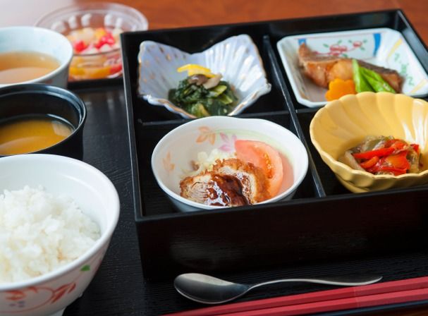 黒いお盆に乗った食事。白いご飯やみそ汁、デザート、4種類のおかずがきれいに盛られている。