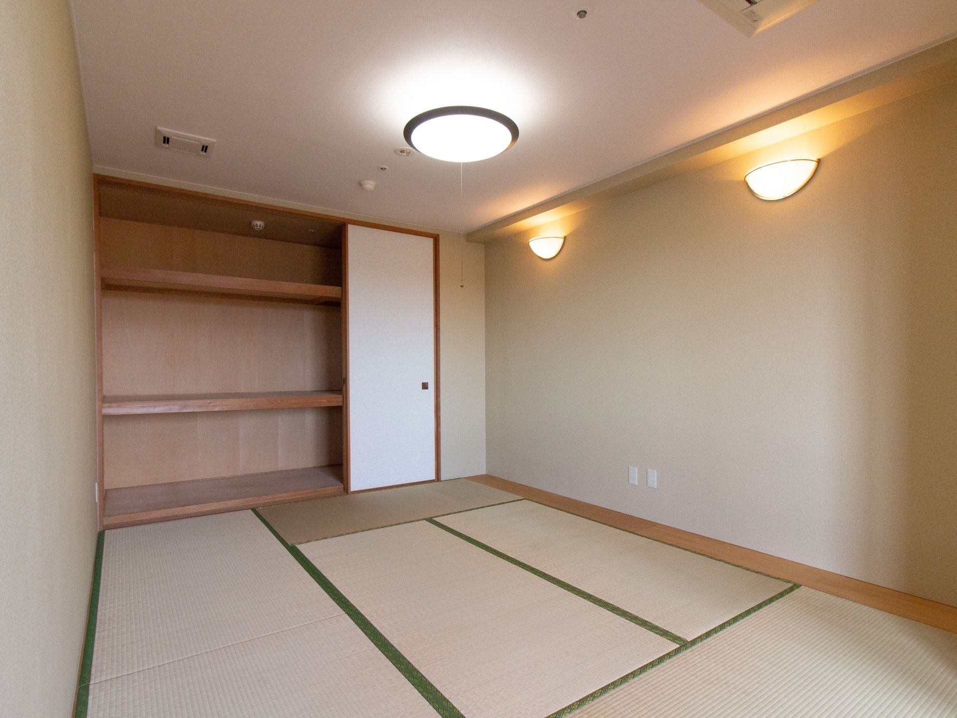 畳が敷かれた広々とした和室には、押し入れが備えつけられている。天井には紐付きの照明が取りつけられている。
