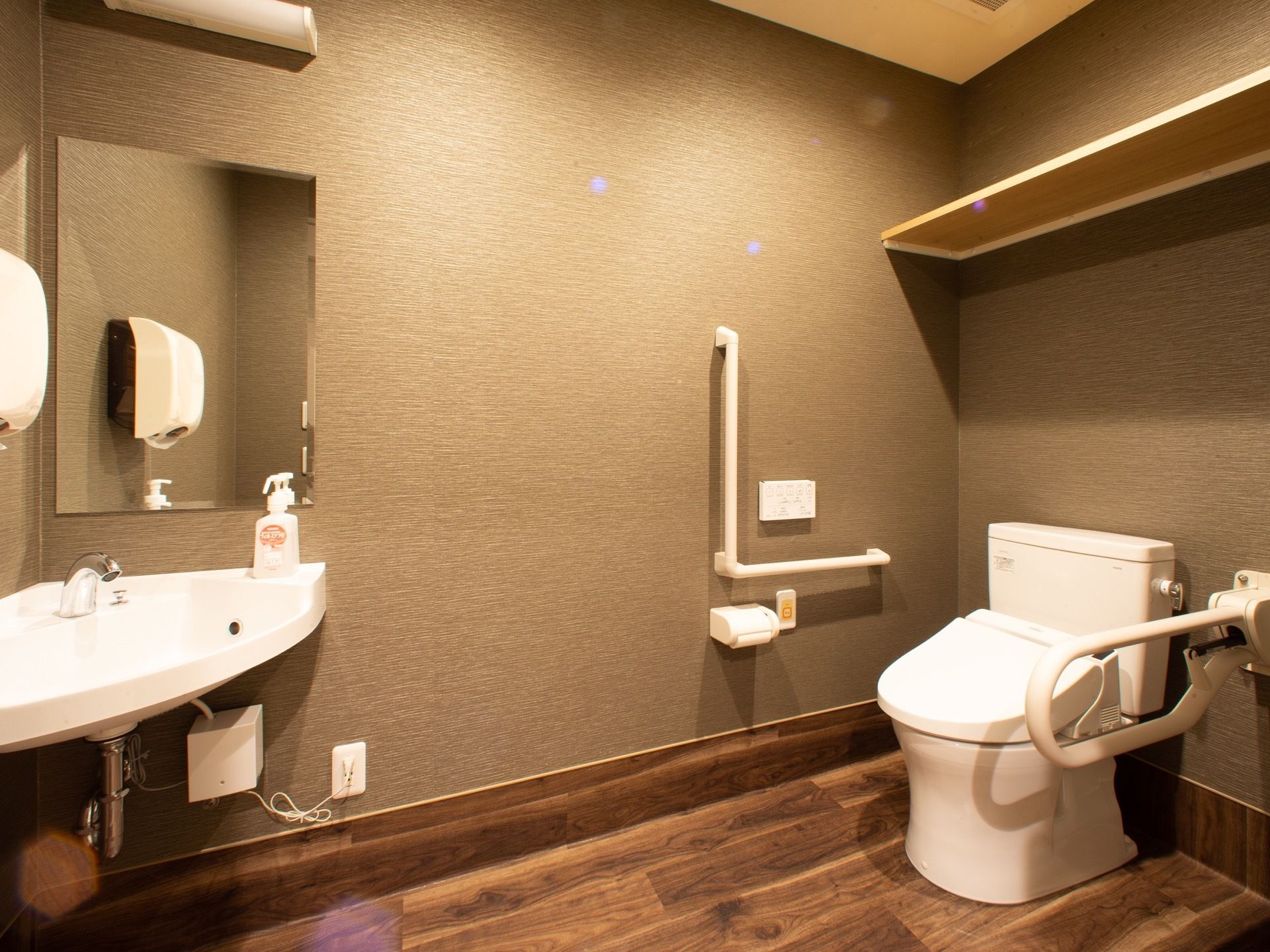 手すりが両側に備わったトイレである。室内に手洗い場が設置されており、横の壁にはペーパータオルがある。