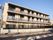 ３階建ての集合住宅が建っている。各部屋にはベランダがついている。建物の前は歩道があり、片側１車線の道路が走っている。