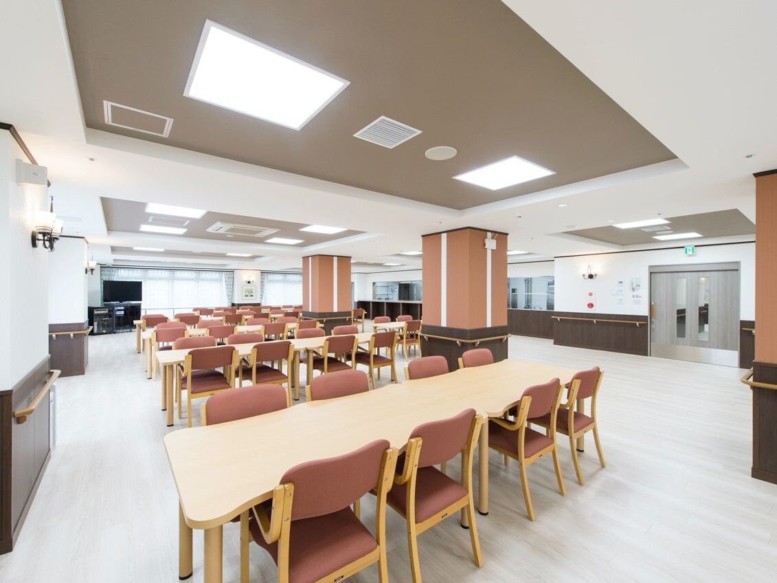 ブラウンの椅子がセットされたテーブルセットが複数ある広い食堂。奥にはテレビも置かれている。