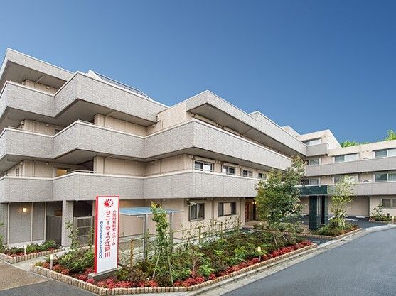 グレー系の大きな他者は各フロアにベランダがあり、敷地内には駐車場と花壇があり、玄関には屋根が付いている。