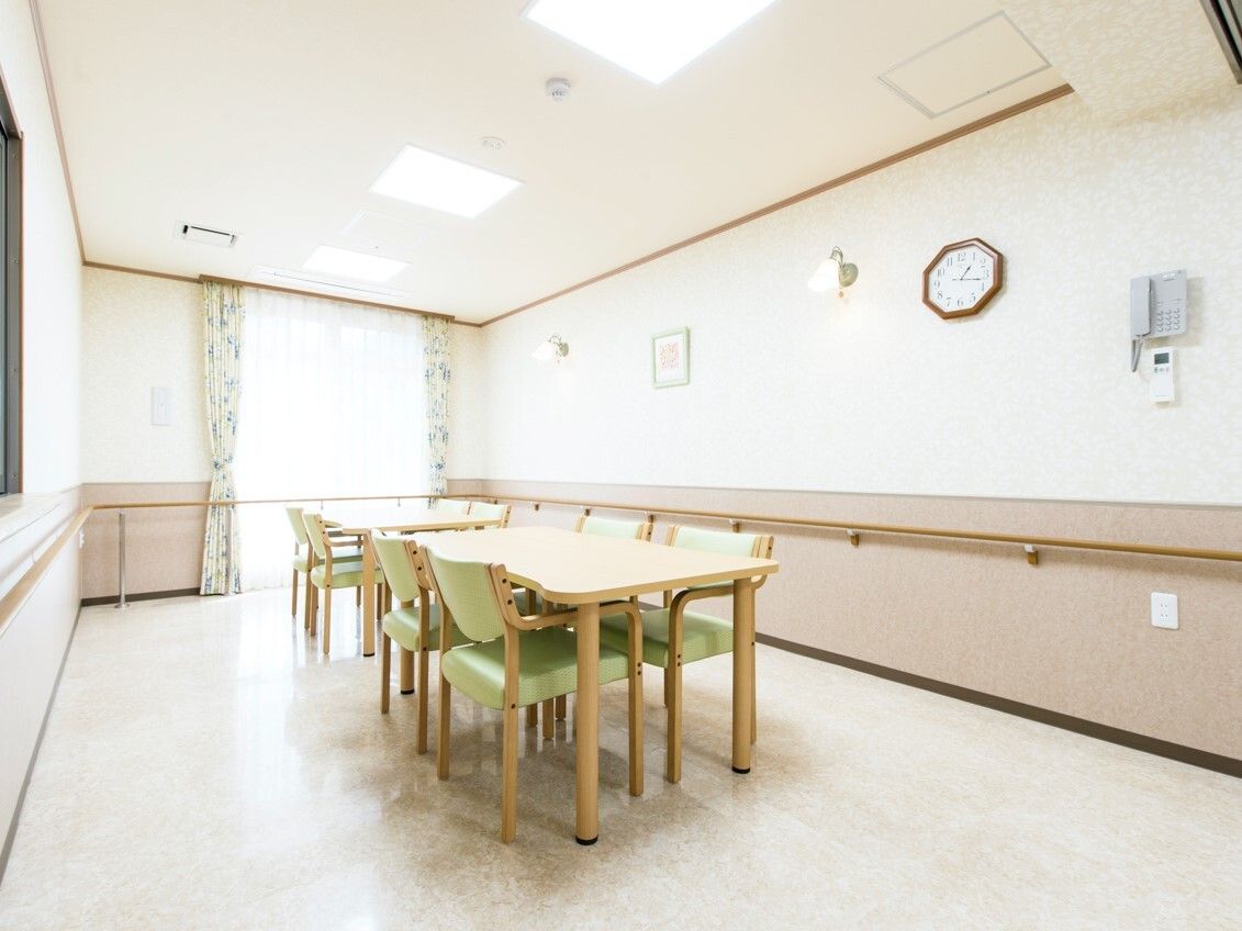 木製のテーブルセットが中央に置かれた共有スペース。壁には手すりが付いていて、窓にはカーテンが付いている。