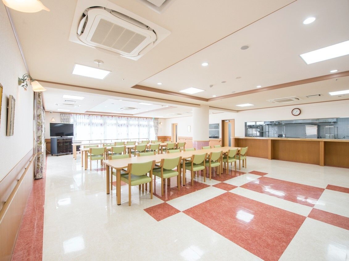 厨房がすぐそばにある食堂にはグリーンの椅子がセットされた木製のテーブルが複数あり、明るい雰囲気。