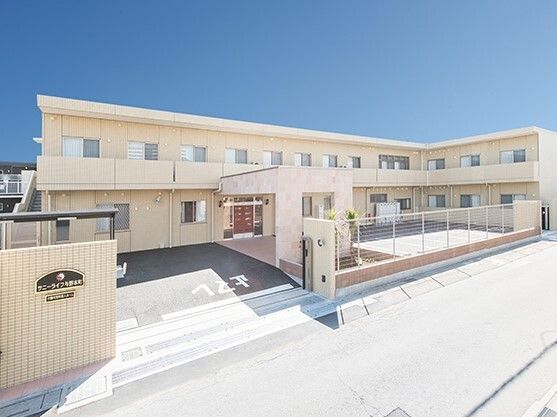 ２階建ての建物はベージュ系の外壁で敷地内には駐車場があり、日当たりのいい場所に建っている。