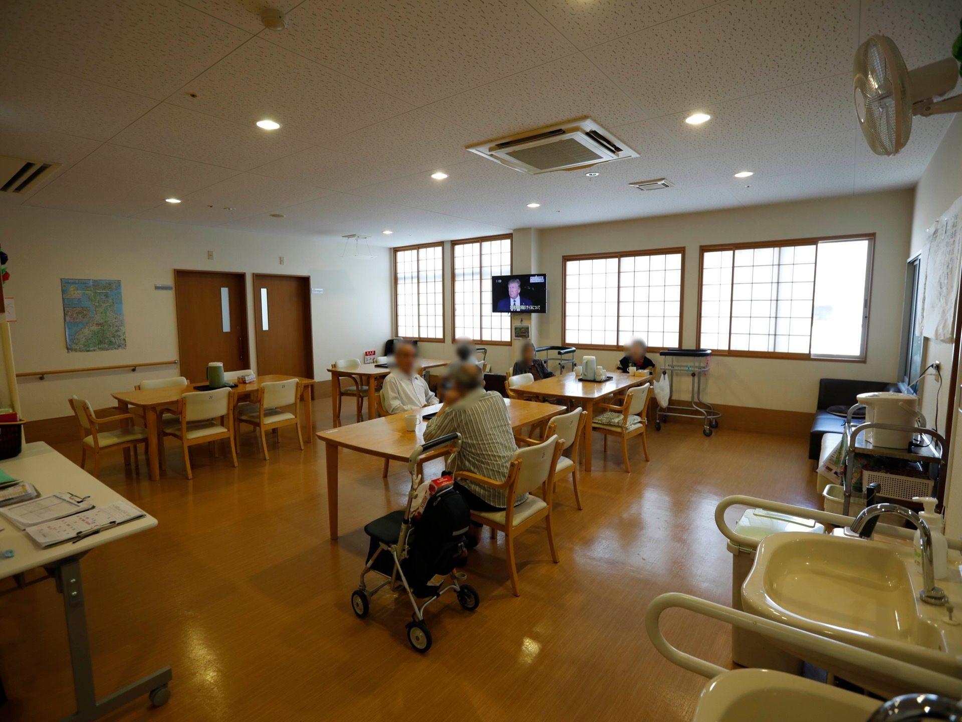 食堂は暖色系の照明が使われており、あたたかみのある雰囲気。複数のテーブルセットが配置されていて、入居者様がくつろいでいる。