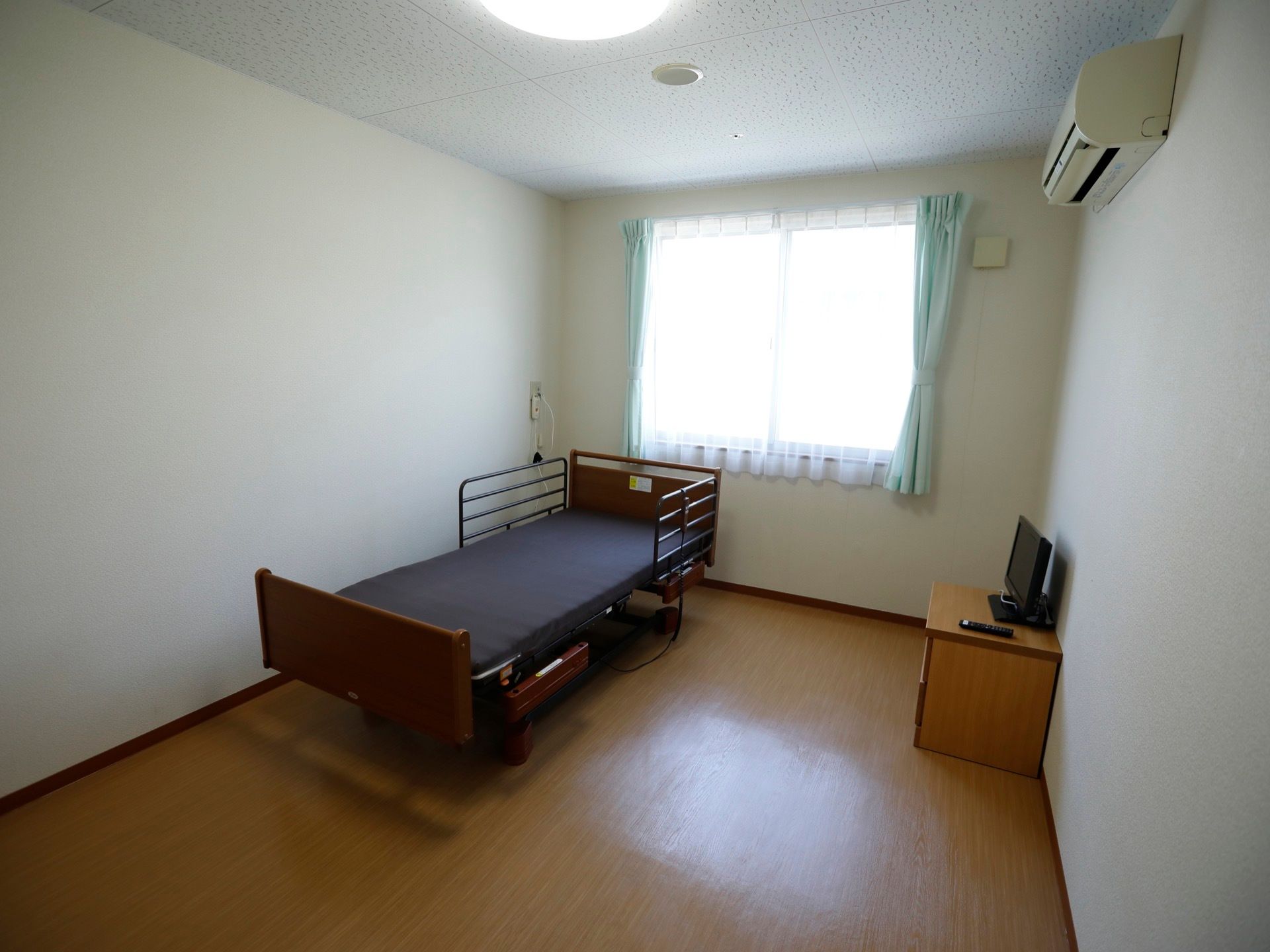 明るく清潔感のある居室は、ワンルームタイプの間取りになっている。介護用ベッドとテレビ、テレビ台が備えられている。