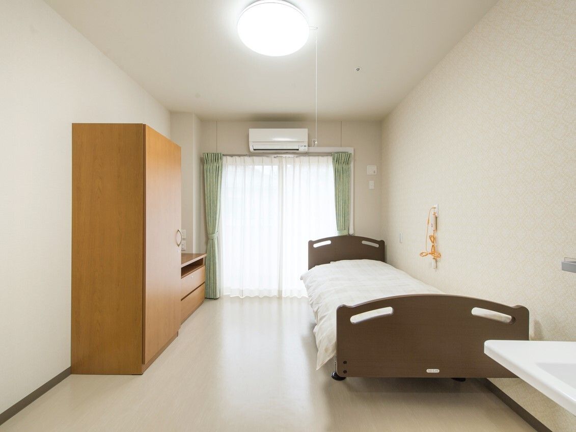 寝具付きのベッドが置かれ、緊急通報装置が付いている部屋にはエアコンや家具も置かれている。