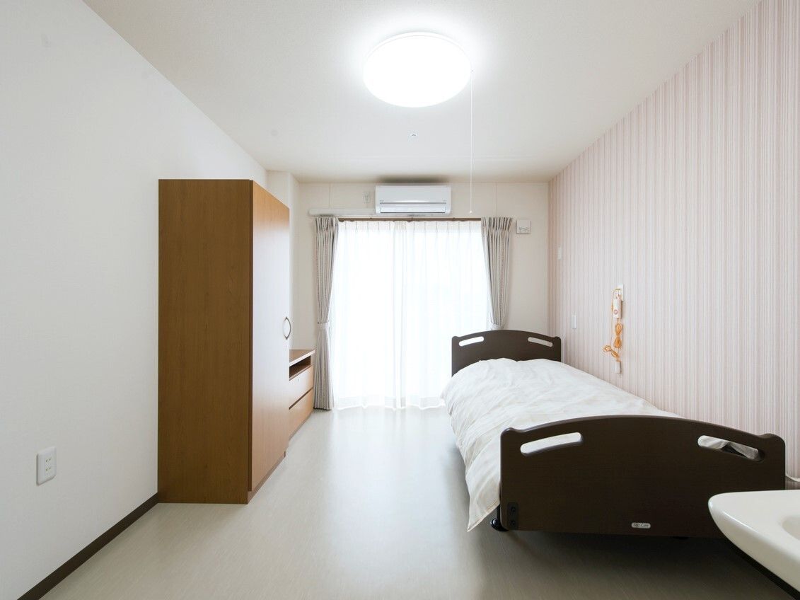 緊急通報装置が付いている部屋にはエアコンや家具も介護ベッドもあり、大きな窓にはカーテンが付いている。