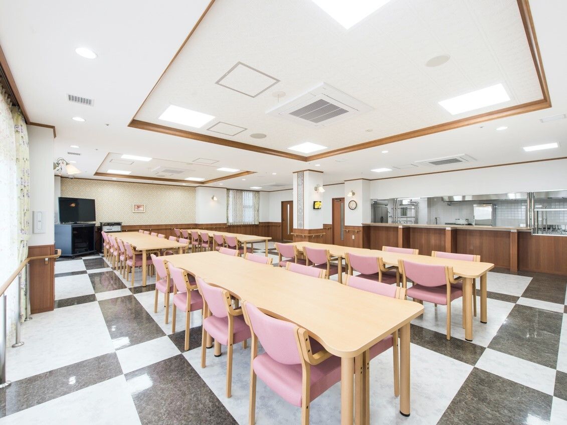 厨房がそばにある食堂にはピンクの椅子がセットされた木製のテーブルセットが多くある。