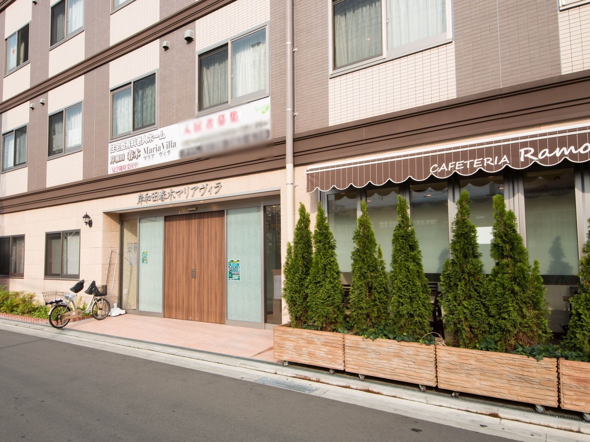 ブラウンとベージュの3階建ての建物は横に長く、大きい。緑も多く植えられている。