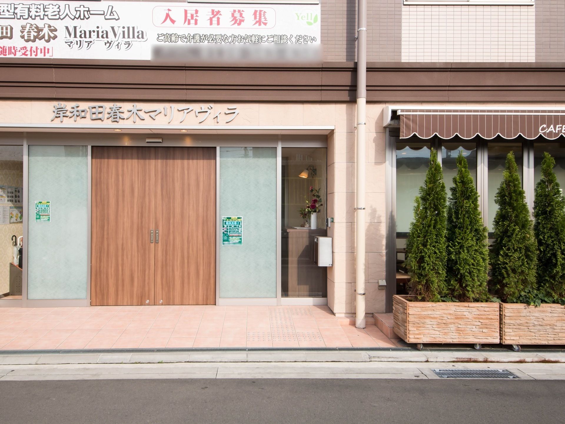 ベージュとブラウンの3階建ての建物は横に長く、エントランス周辺にはたくさんの木が植えられている。