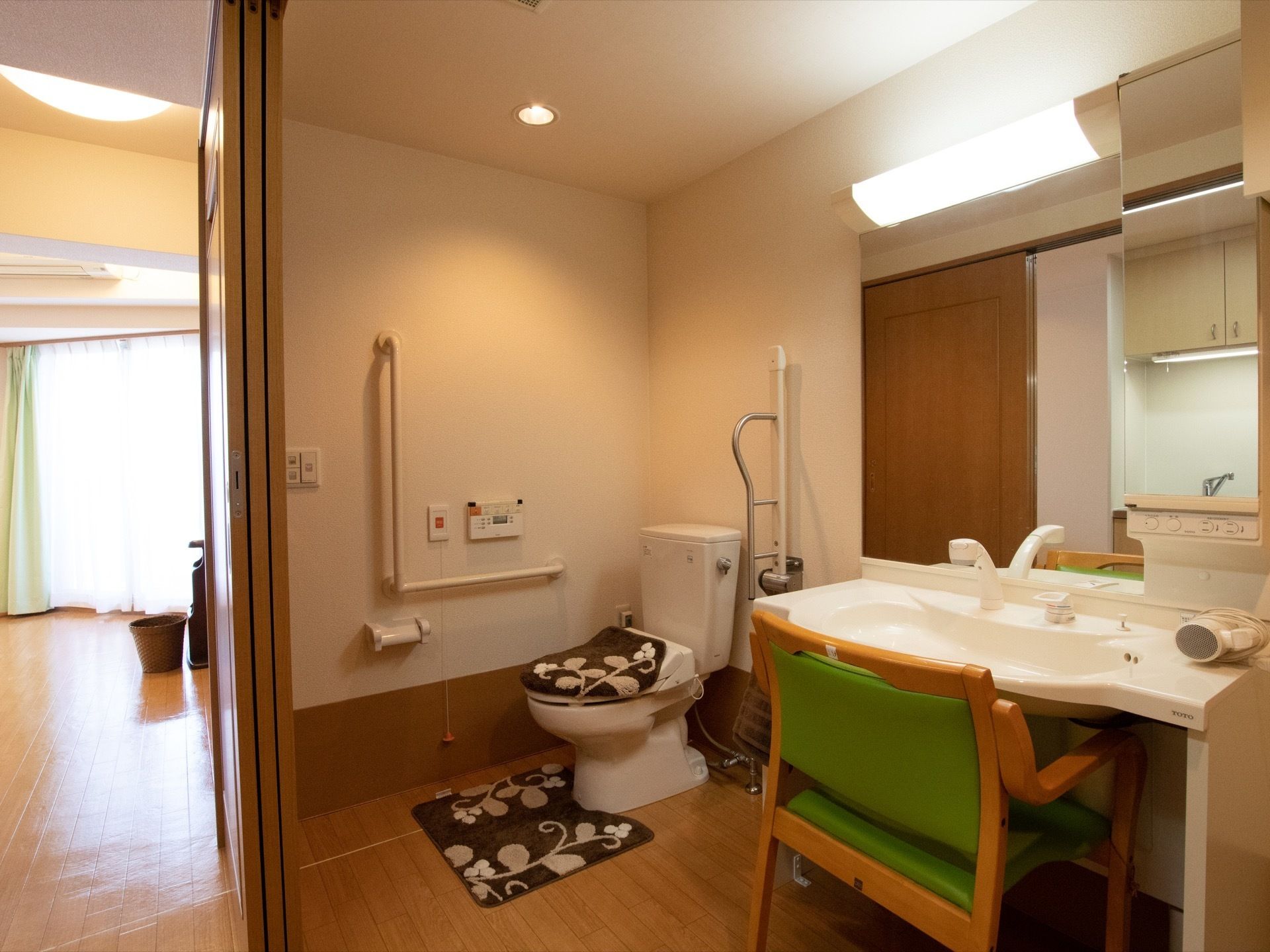 居室の一画に引き戸で仕切られたトイレと洗面台がある。トイレの周囲には手すりやナースコールが設けられ、洗面台の前には椅子が置かれている。