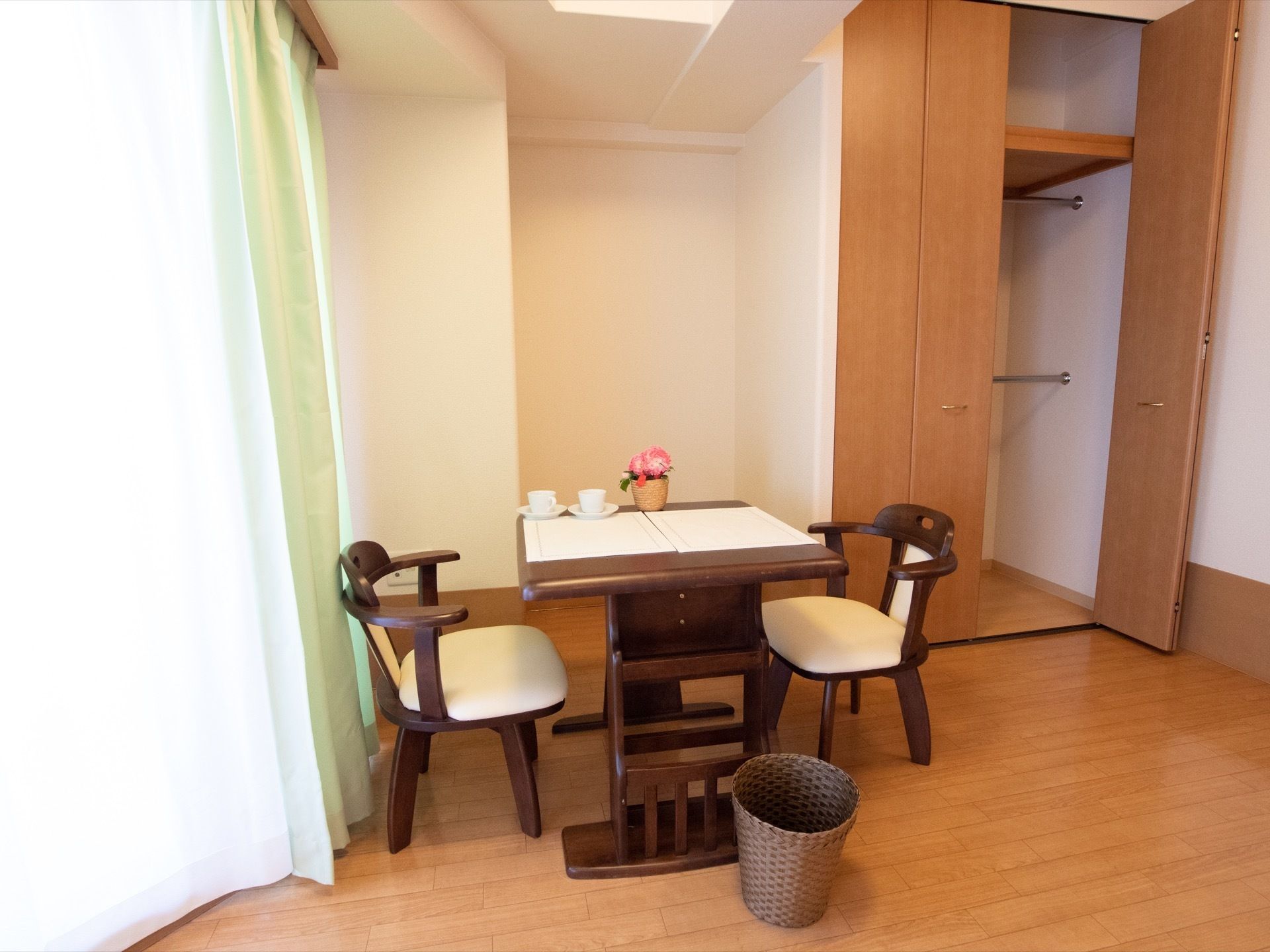 大きな窓のあるフローリングの部屋に、テーブルと椅子が置かれていて、部屋の奥の壁には、作りつけのクローゼットがあるのが見える。