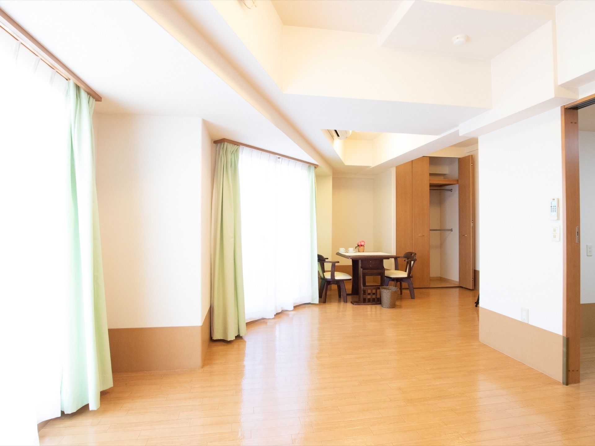 日差しの差し込む大きな窓が複数ある広い居室。右側には他の部屋への入口があり、部屋の奥にはエアコンやクローゼットが備えつけられている。