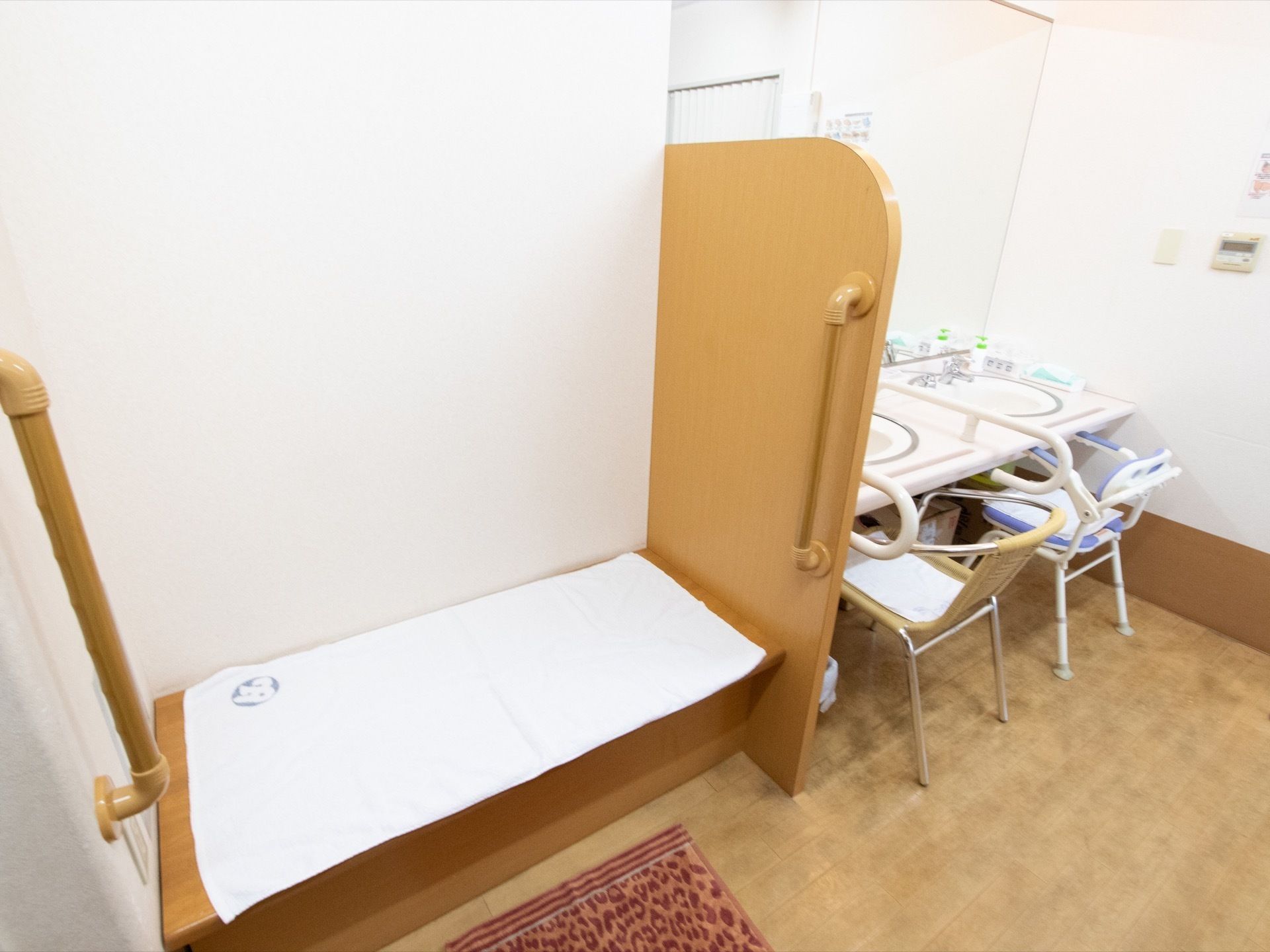 浴室に設置されているベンチや洗面台。ベンチと洗面台には手すりがついていて洗面台の前には椅子が置かれている。